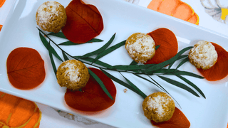 Six golden-brown mini pastries dusted with white powdered sugar, arranged on a white rectangular platter with orange autumn leaves and green sprigs.