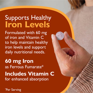 A close-up of a hand holding a round silver supplement tablet, with a large brown promotional graphic behind it. The text reads: 'Supports Healthy Iron Levels' and details about 60 mg iron and Vitamin C.