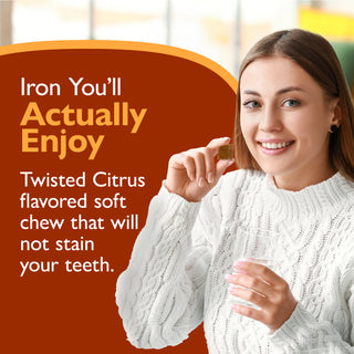 A smiling woman in a white cable-knit sweater holds a small brown chewable tablet next to promotional text on a dark orange background. The text reads: 'Iron You'll Actually Enjoy Twisted Citrus flavored soft chew that will not stain your teeth.